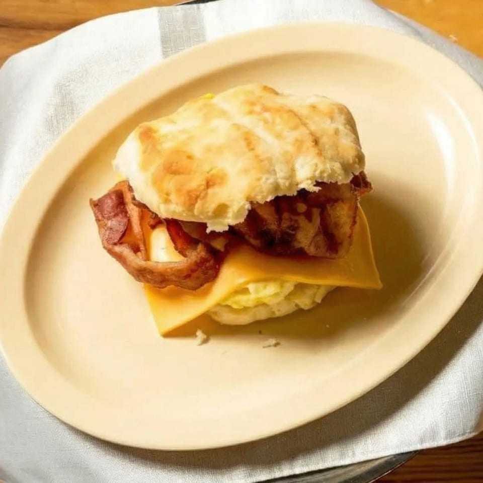 A breakfast sandwich with bacon, egg, and cheese on a biscuit, served on a yellow plate.