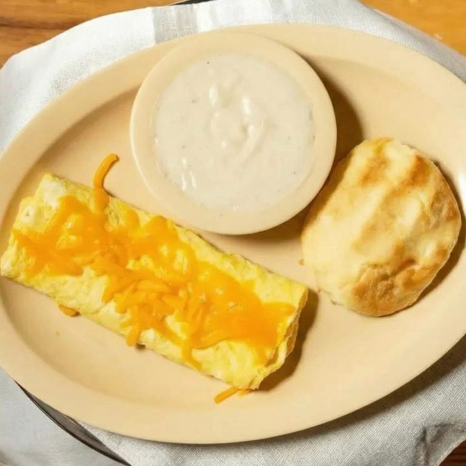 A cheese omelet, biscuit, and a bowl of gravy on an oval plate.